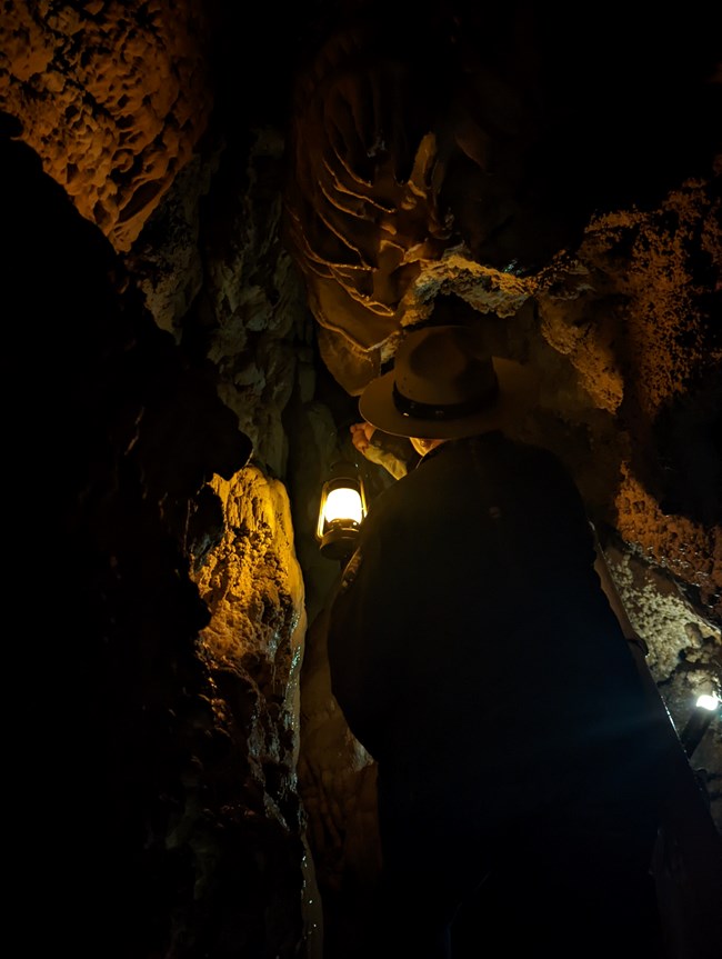 Ranger holds a lantern illuminating narrow cave walls