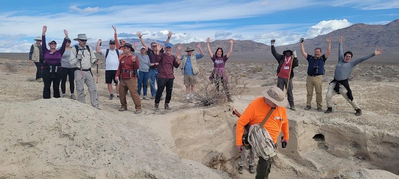 A group of visitors posing with their hands raised among tan badlands.