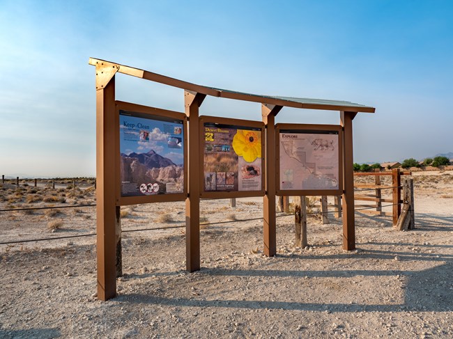 An exhibit kiosk in front of a wooden fence and desert landscape.