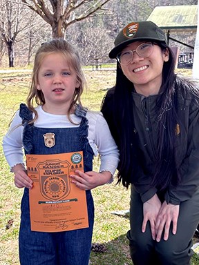 Young girl stands next to park ranger holding a Junior Ranger certificate