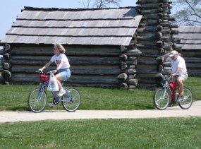 Two people bike past reconstructed huts on the Valley Forge Joseph Plumb Martin trail.