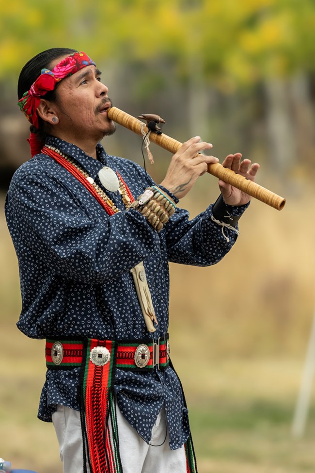 A Native American flute player looks up toward the sky as he plays.