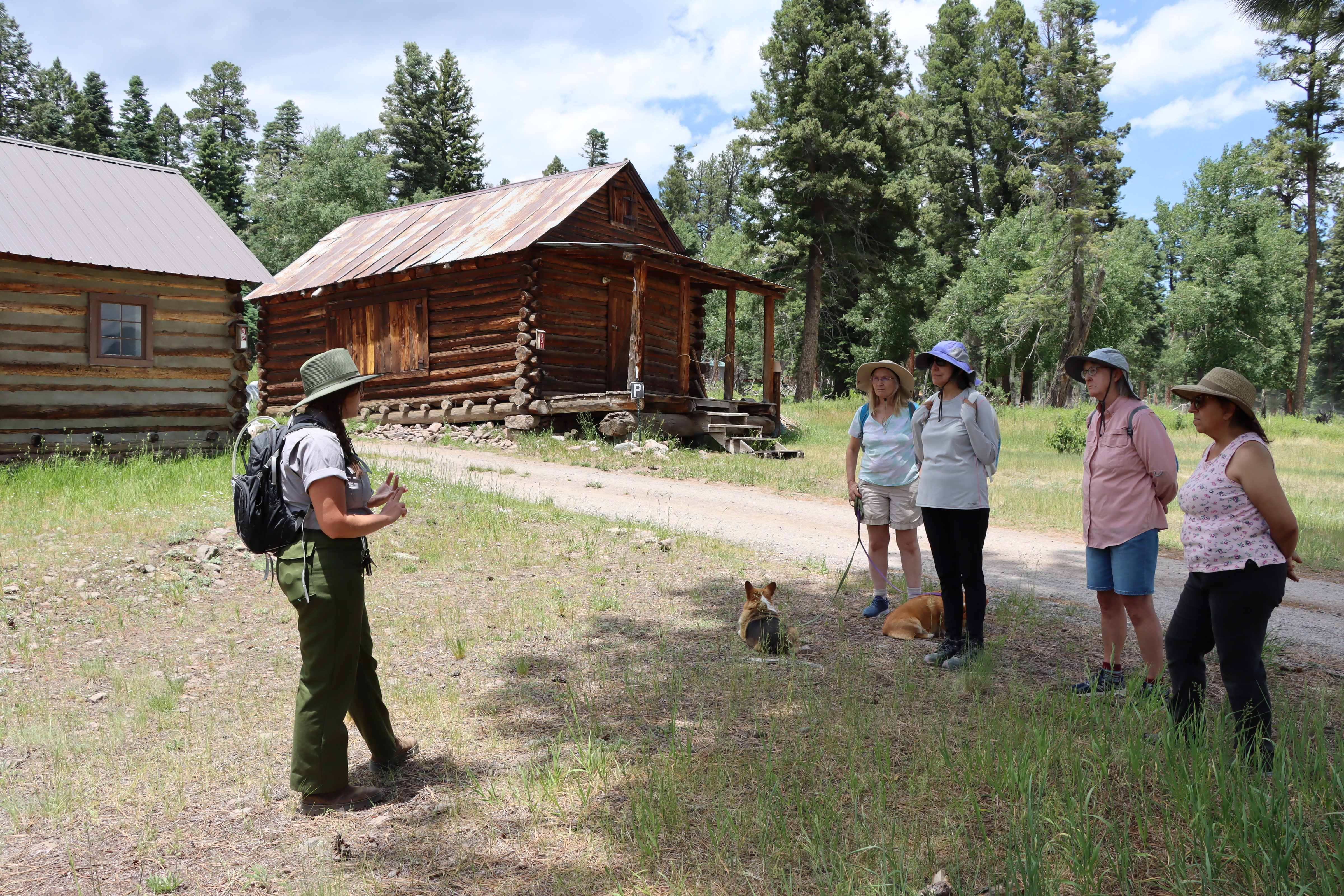 Ranger and several visitors standing and talking near rustic, wooden cabins