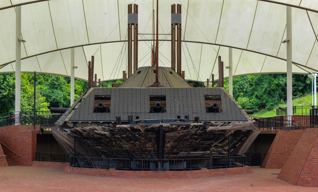 A large black and wooden gunboat sits under a large covering
