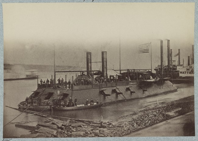 A black and white image of the large gunboat in the river with staff on upper and lower decks