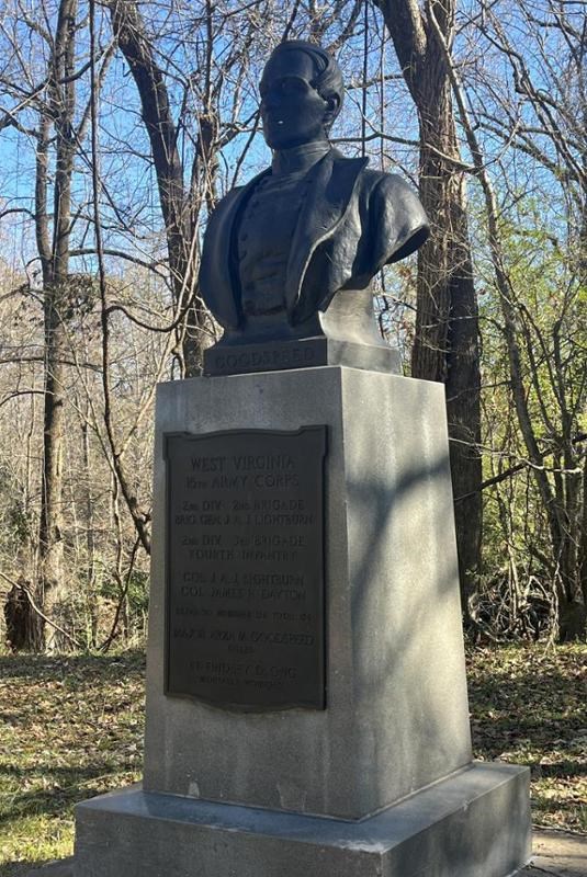 bronze bust of man in military uniform against a wooded background