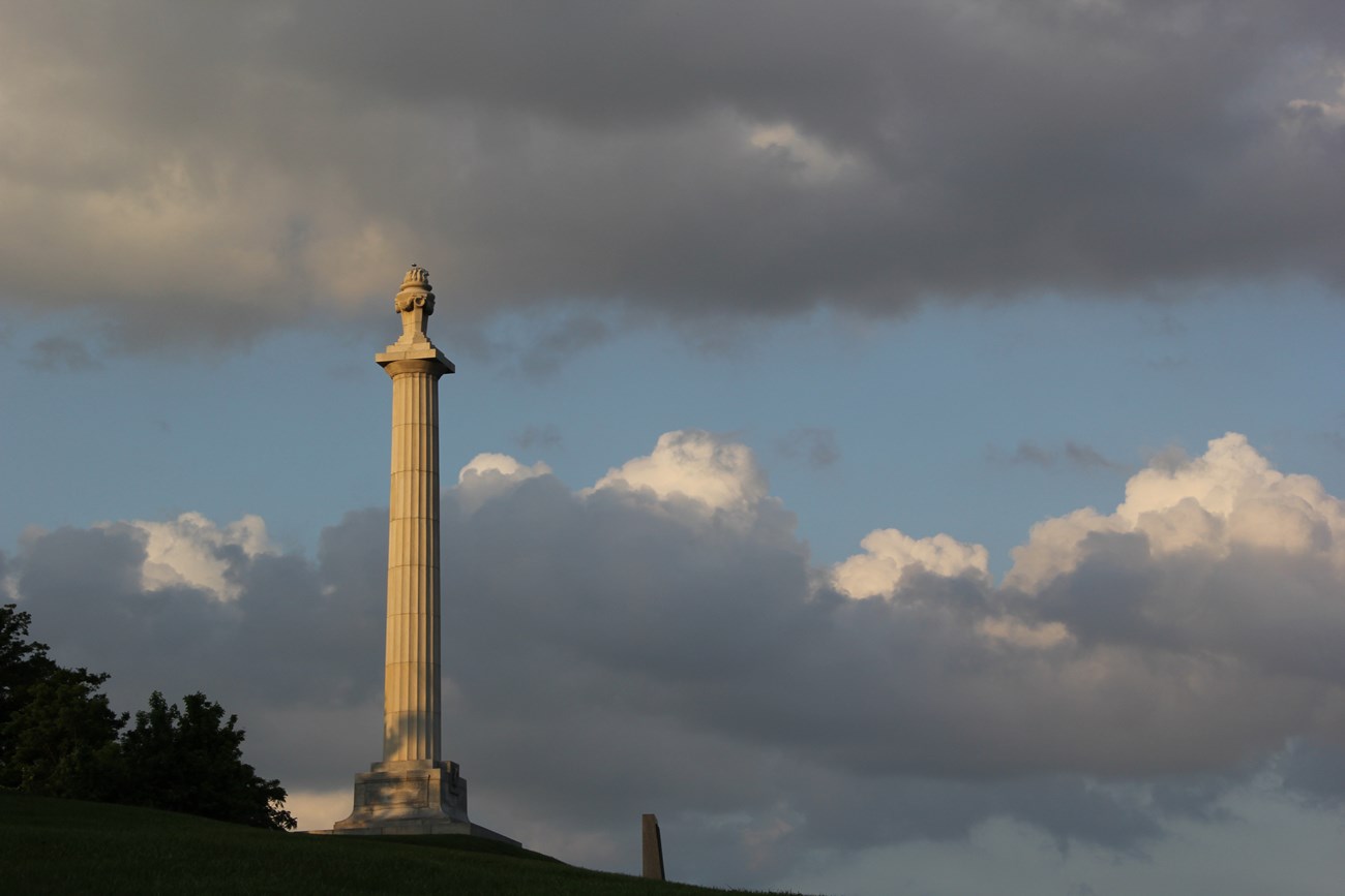 A tall column sits atop a hill with a sculpture of an eternal flame on the very top