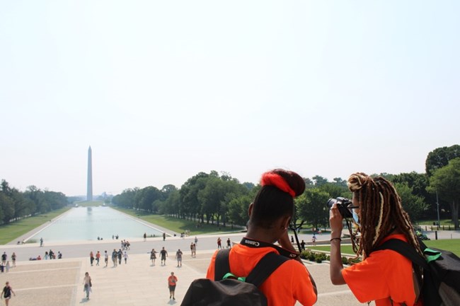 Two girls take a photo of the Washington Monument from the Lincoln Memorial.