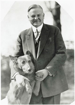 Herbert Hoover smiles for the camera holding his dog's paws.