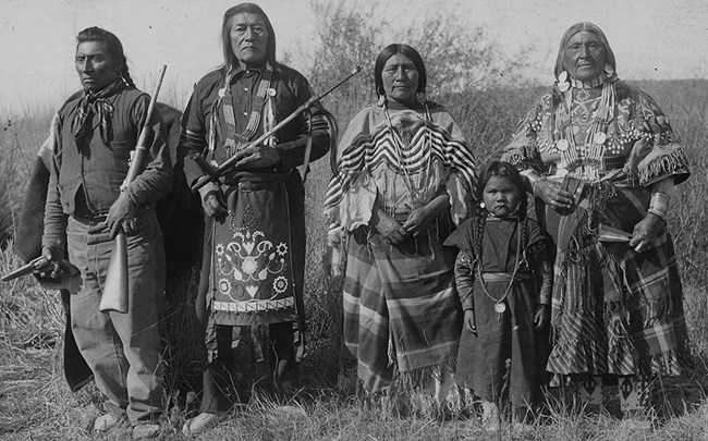 Historic image of family group of four tribal members wearing traditional clothing