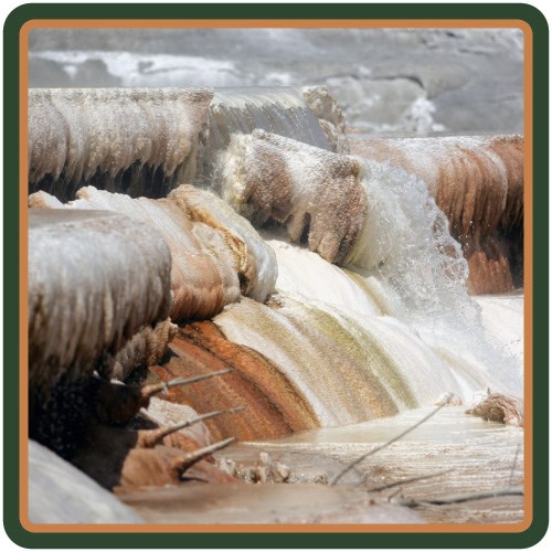 Close-up view of water flowing down white, yellow, and orange-colored travertine terraces.