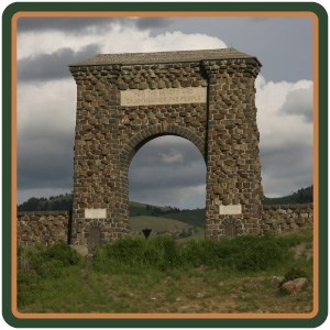 The stone Roosevelt Arch standing above a hillside of grasses and shrubs.