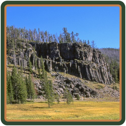 A jagged, gray cliff rises above a wetland and meadow.