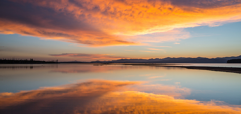 A multitude of reds, yellows, and oranges as the sun rise over a lake.