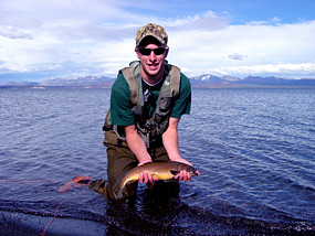 Angler kneeling in Yellowstone Lake and holding cutthroat trout with Absaroka Mountains in the background.