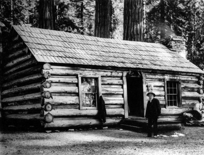 Galen Clark standing in front of a log cabin.