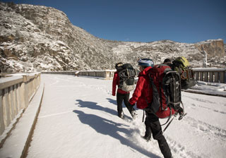 Hikers walking across snow-covered dam toward hills