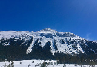 Snowy mountain with several avalanche chutes and snow blowing in the wind