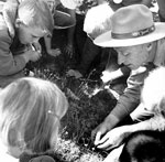 Ranger leans down to show children plant in historic photo