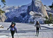 Two people cross-country ski with Half Dome in background