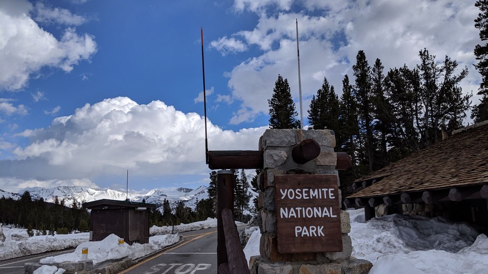Yosemite National Park entrance sign at Tioga Pass with snowy mountains and plowed road in background