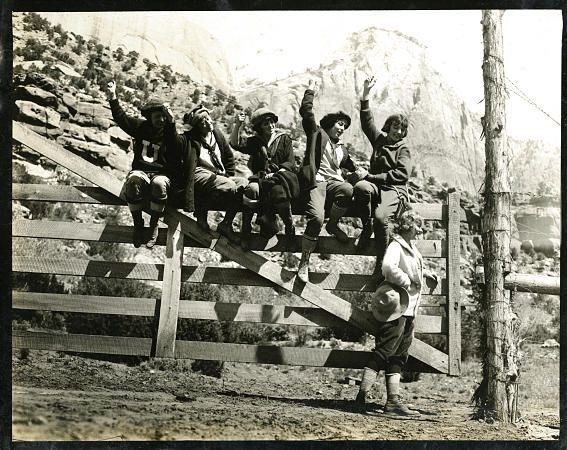Students Ann Widtsoe, Mildred Gerrard, Nell Creer,  Melba Dunyon and Dora Montague, wave as they sit top of a fence gate. Chaperone Catherine Levering stands nearby