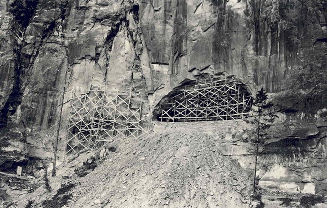 Wooden scaffolding next to holes being dug in rock on the side of a cliff