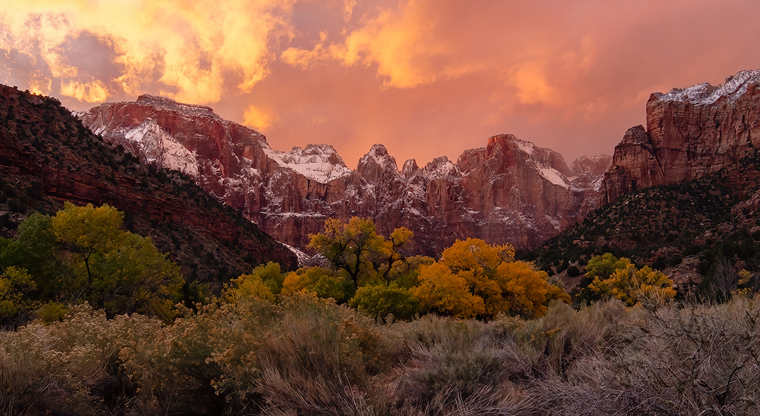 Clouds glowing pink, over red cliffs dusted with snow.