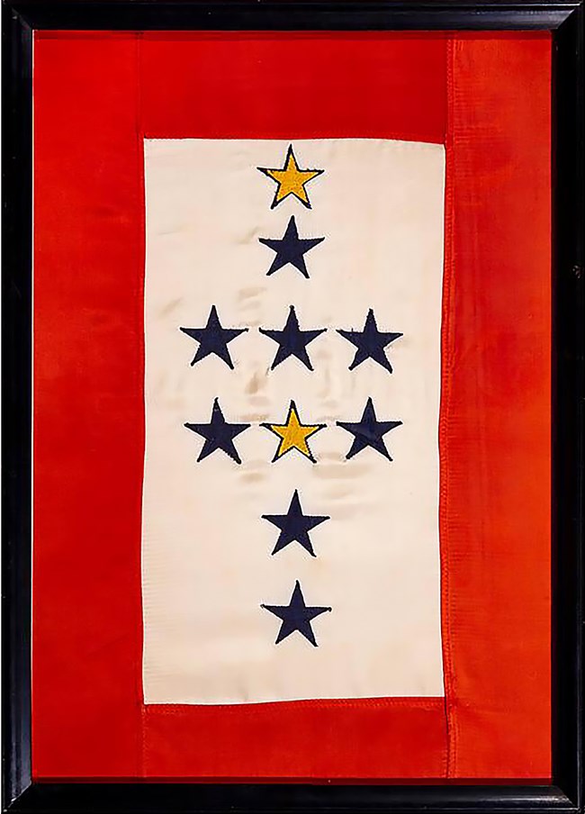 Service flag honoring staff of the Franklin D. Roosevelt Library who served in the military during World War II, 1945. Collection of the Franklin D. Roosevelt Presidential Library and Museum (MO 1969.51). Framed fabric service flag. A wide border of red frames a collection of 2 gold and 8 blue stars on a white background.