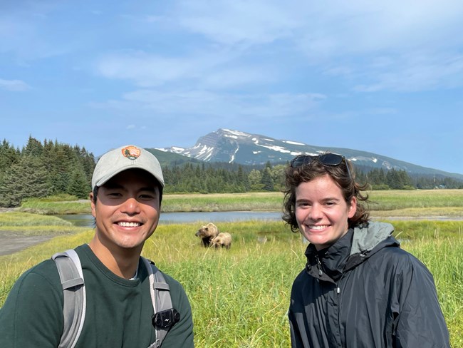 Two BPI interns in a meadow with bears, a lake, and a mountain behind them