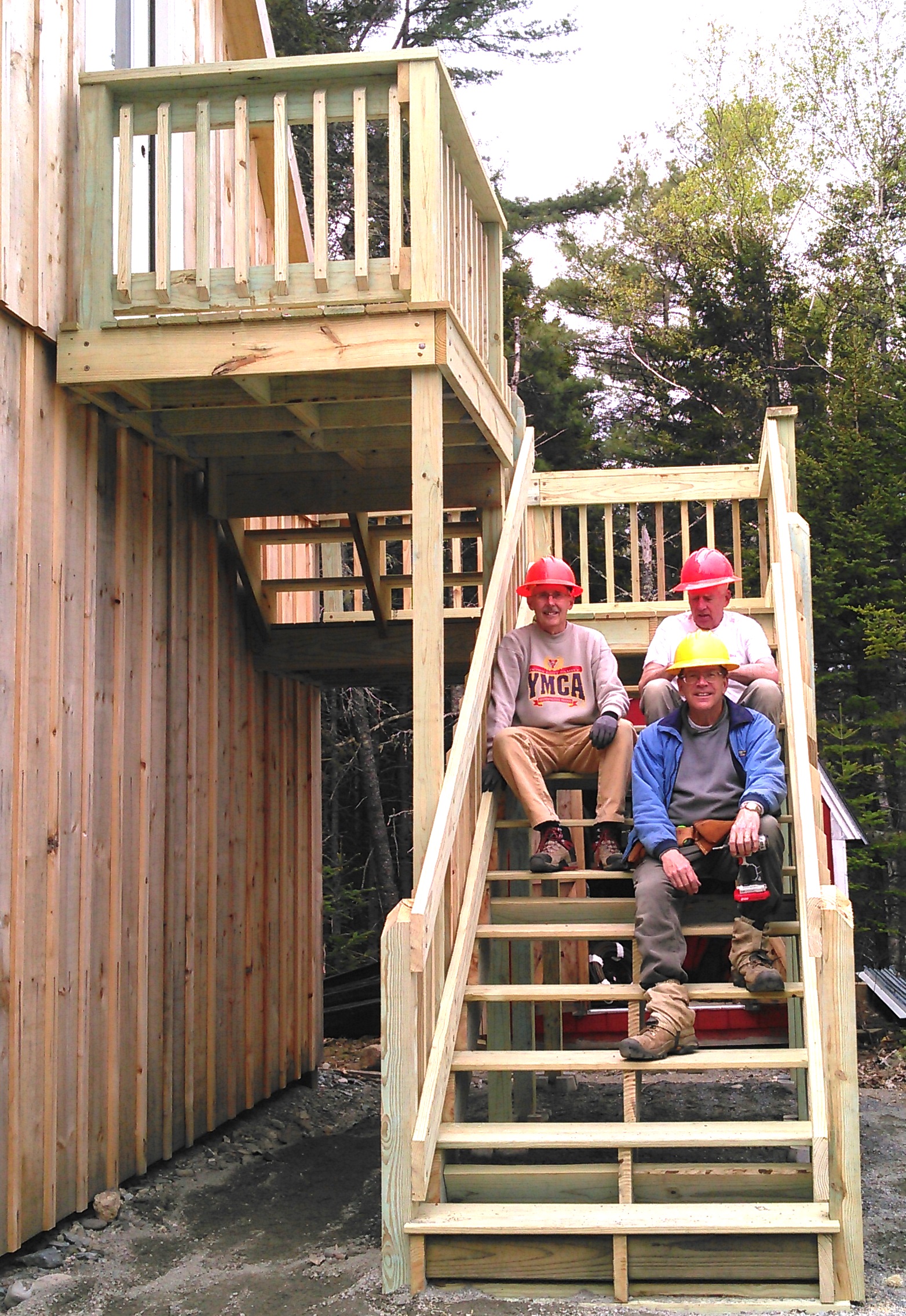 Three middle age men set facing the camera on bright wooden steps.