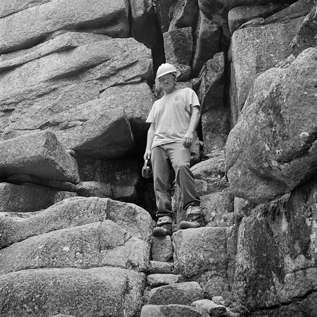 Black and Photograph of a trail crew worker with large rocks in the back ground.