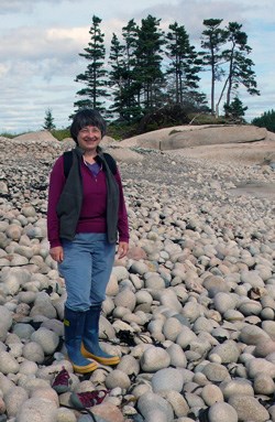 Woman standing on large shoreline rocks with tall trees in background