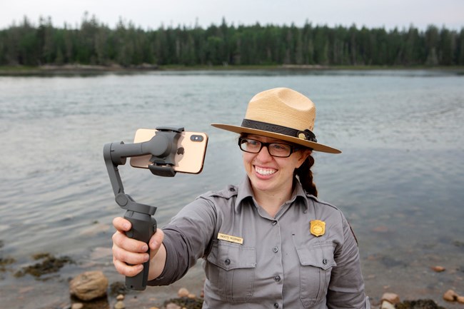 Park ranger stands on a beach while recording herself with a smartphone