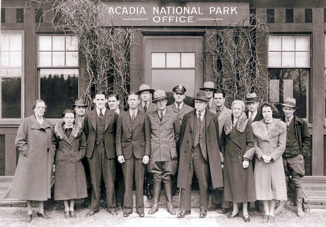 a mix of men and women in B&W stand in front of a park building