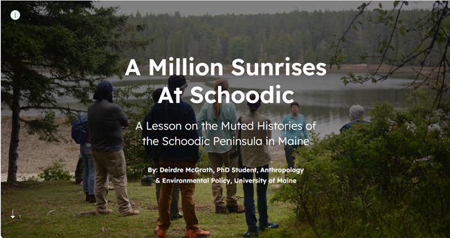 Group of people standing in a wooded area facing a coastal shoreline listens to a woman who is speaking to them while holding a large map in one hand
