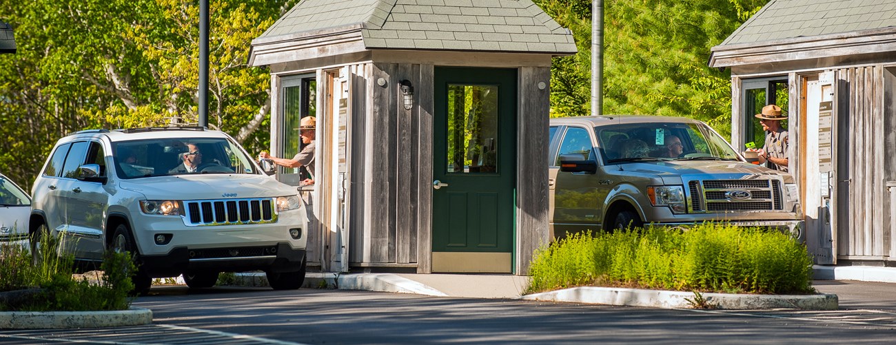 Two roadside booths where park rangers speak with drivers of cars lined up to pay entrance fees