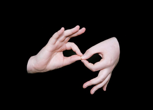 Against a black background, two hands gesture a symbol in American Sign Language