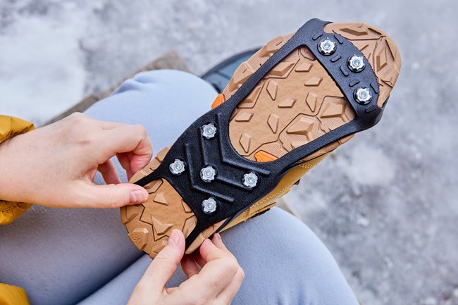 Close photo of hands attaching icy traction devices to winter boots