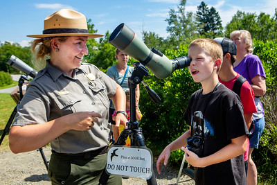 Child looks through a spotting scope with ranger assistance