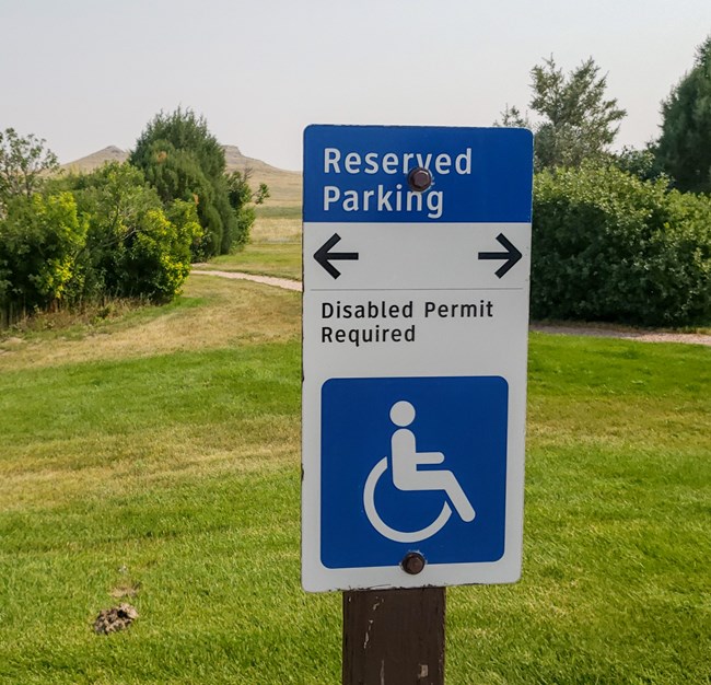 Blue and white parking sign with wheelchair icon. Text reads Reserved Parking disabled permit required.