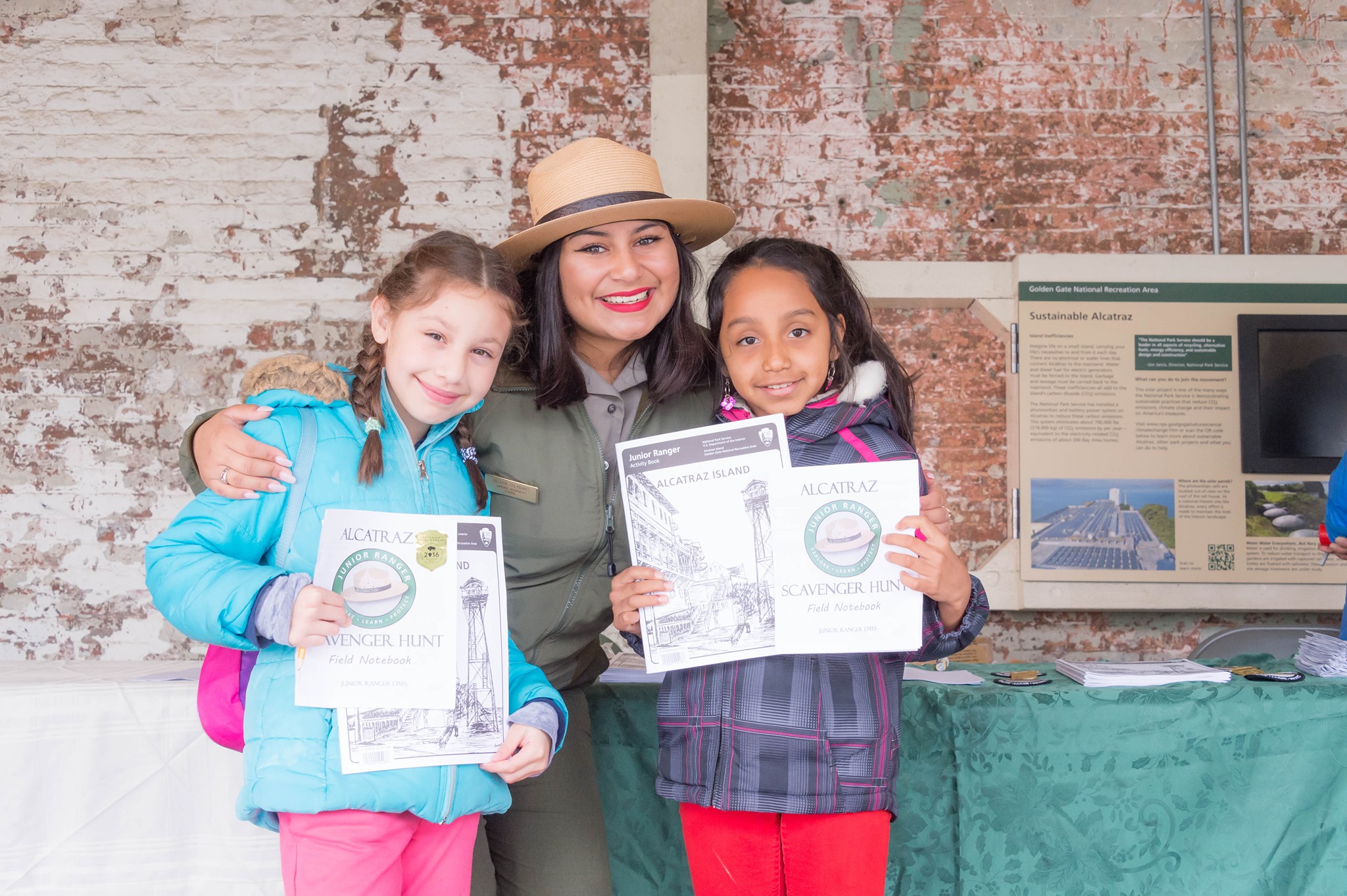 Park Ranger stands between two girls holding Junior Ranger Books.