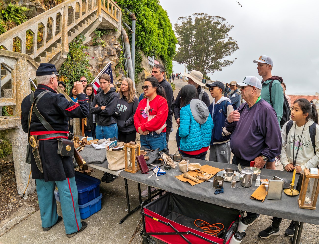 Man in blue Civil War uniform talks to a crowd. Table displays various historic objects.