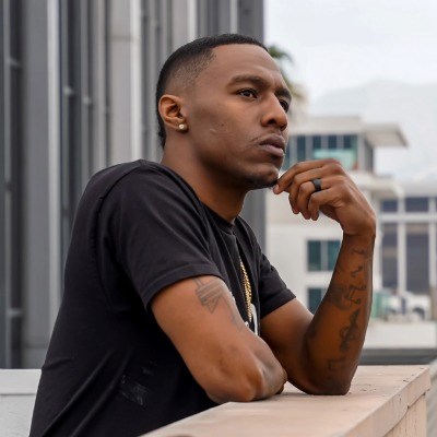 African American man leans against a balcony, chin rested thoughtfully on his hand.