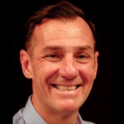 White man in white collard shirt smiles at camera
