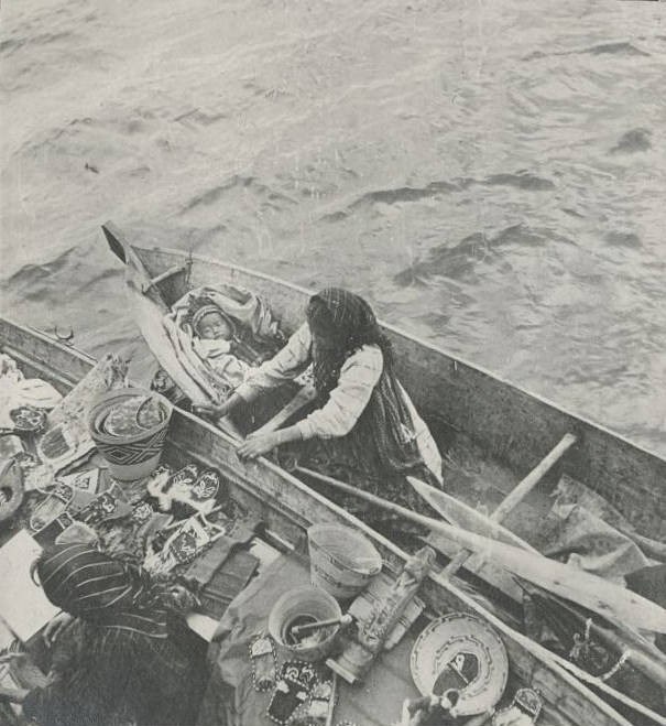 a woman in a boat packed with crafts and goods as well as a baby