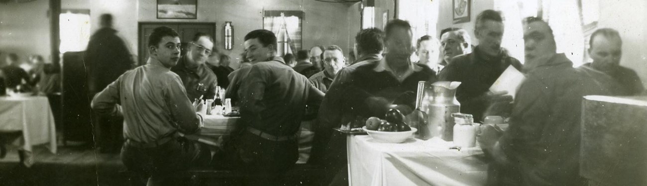 a historic scene of a military dining hall in which men sit and eat dinner at long tables.