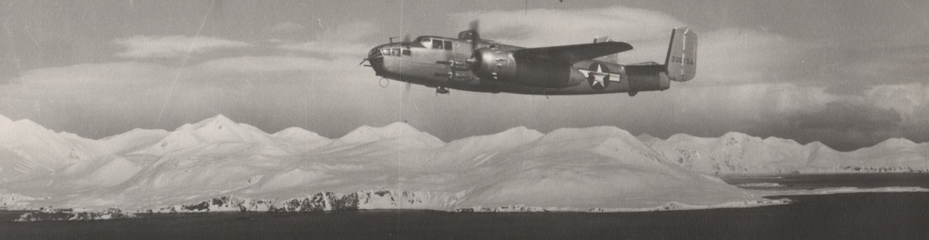 a historic scene of a propeller plane with a large star flying over a snowy coastal mountain range.