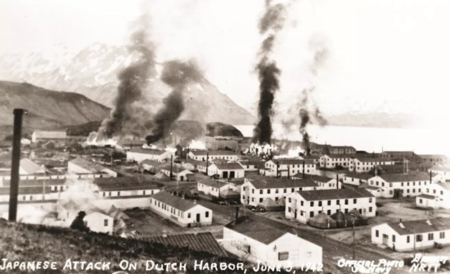 a historic scene of a seaside town with numerous homes on fire.