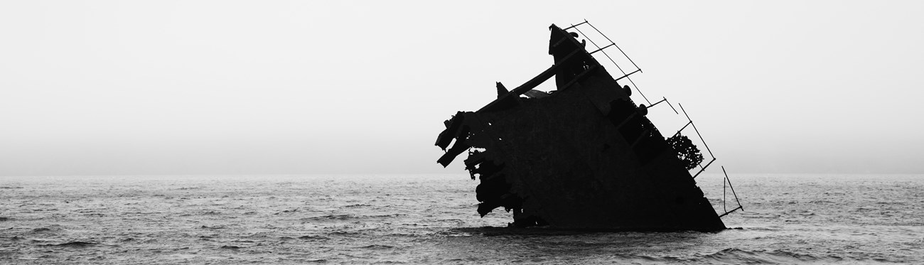 the nose of a wrecked ship silhouetted against the foggy white background of the Pacific ocean.